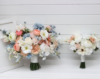 Puede incluir: Dos ramos de novia con flores de melocotón, blancas y azules. El ramo más grande tiene una cinta de satén blanca. El ramo más pequeño tiene una cinta de satén blanca.