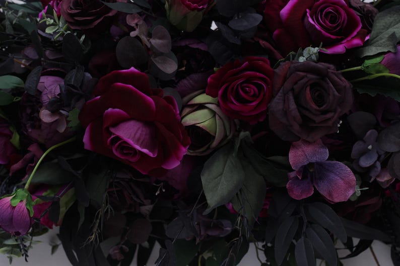 May include: A bouquet of deep purple and burgundy roses, with green leaves and other flowers, arranged in a lush, romantic style.