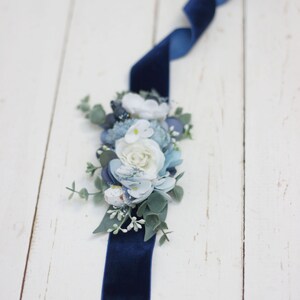 Pu&ograve; includere: Un nastro di velluto blu navy con un gruppo di fiori di stoffa blu e bianchi e del verde.
