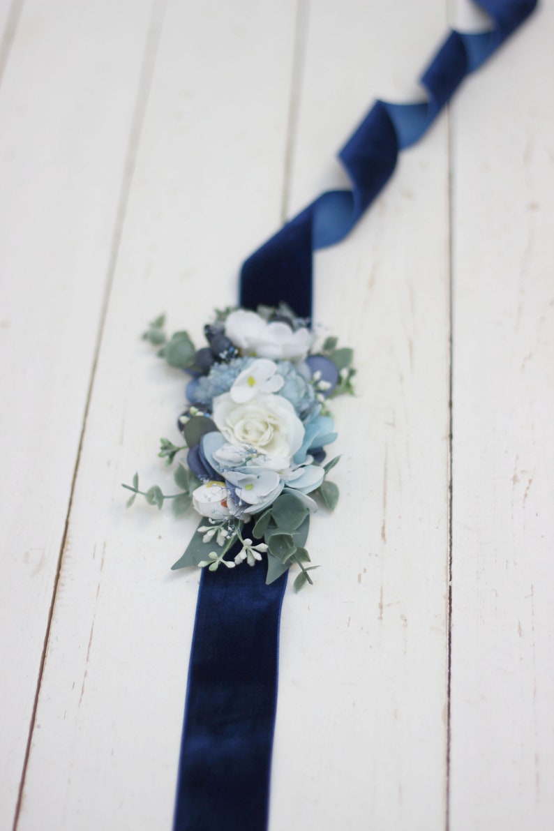 Pu&ograve; includere: Un nastro di velluto blu navy con un gruppo di fiori di stoffa blu e bianchi e del verde.