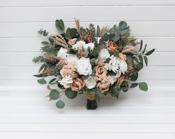 May include: A bouquet of faux flowers in shades of white and beige, featuring roses, eucalyptus, and dried grasses. The bouquet is tied with a brown ribbon.