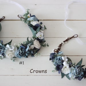 Pu&ograve; includere: Due corone di fiori con fiori bianchi e blu e verde. La corona a sinistra &egrave; etichettata #1 e la corona a destra &egrave; etichettata #2. Corone.
