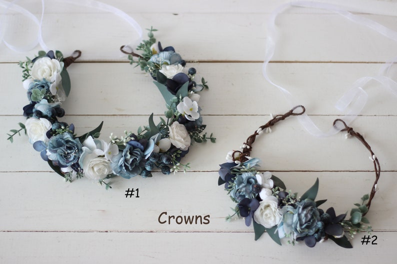 Pu&ograve; includere: Due corone di fiori con fiori bianchi e blu e verde. La corona a sinistra &egrave; etichettata #1 e la corona a destra &egrave; etichettata #2. Corone.