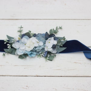 Pu&ograve; includere: Un nastro di velluto blu navy con un abbellimento floreale. L'abbellimento presenta fiori bianchi, blu e verdi.