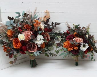 May include: Two bouquets of artificial flowers in shades of orange, red, and pink. The larger bouquet is tied with twine and the smaller bouquet is tied with a green ribbon.
