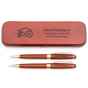Può includere: Un set di penna e matita in legno con dettagli dorati, presentato in un astuccio in legno abbinato. L'astuccio è inciso con un'icona di cappello di laurea e ingranaggio, insieme al nome "Jamal Washington", dettagli universitari e l'anno 2025.