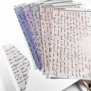 Könnte beinhalten: Ein Set aus sechs abreißbaren Washi-Tape-Blättern mit einem Vintage-Schriftdesign. Die Blätter sind in verschiedenen Rosatönen, Lila und Blau gehalten. Der Text auf den Blättern lautet "PoseColored Daze" und enthält eine handschriftliche Schrift.