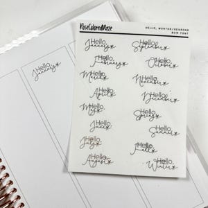 May include: A sheet of clear stickers with handwritten text in a cursive font. The stickers feature the words "Hello" followed by the months of the year, seasons, and the words "Spring", "Summer", "Autumn", and "Winter".