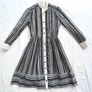 May include: A black and white striped dress with a white collar and cuffs. The dress has a button-up front and a fitted waist. The skirt is a-line and falls to the knees.