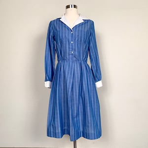 Peut inclure: Une robe à rayures bleues et blanches avec un col blanc et des manches longues. La robe a un corsage ajusté et une jupe ample.