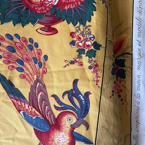 May include: Yellow fabric with a floral and bird design. The fabric features a parrot with red, blue, and white feathers, and a vase of red and white flowers. The fabric also has text that reads "par Frelle, imprim&eacute; &agrave; la main, marque et mod&egrave;le d&eacute;pos&eacute;s".