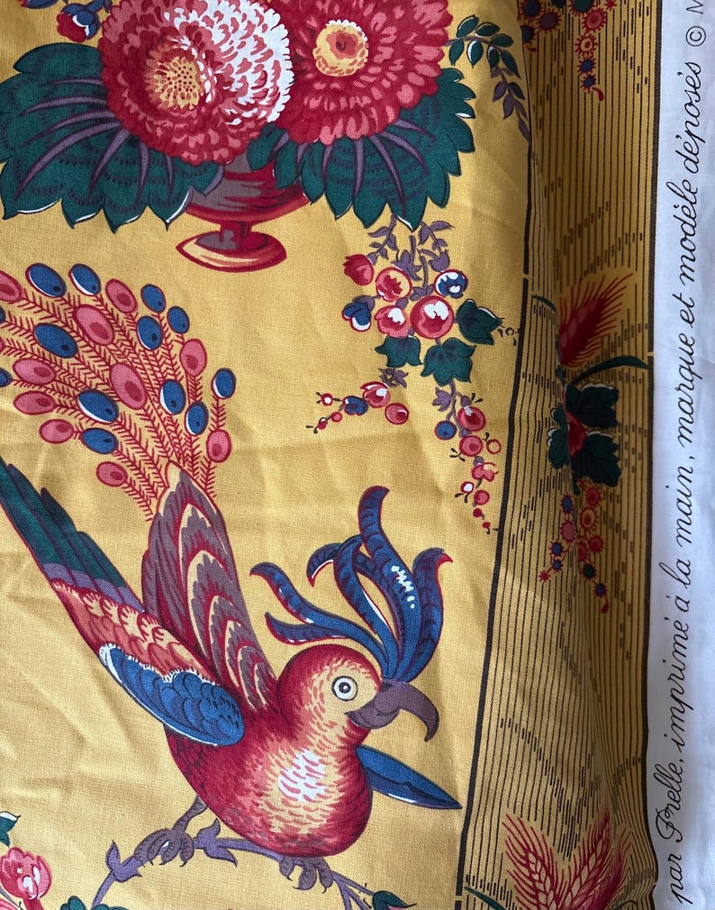 May include: Yellow fabric with a floral and bird design. The fabric features a parrot with red, blue, and white feathers, and a vase of red and white flowers. The fabric also has text that reads "par Frelle, imprim&eacute; &agrave; la main, marque et mod&egrave;le d&eacute;pos&eacute;s".