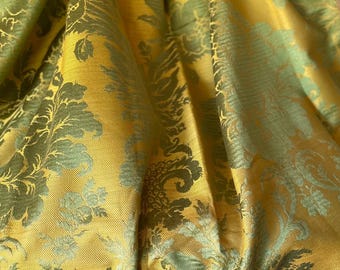 Può includere: Un tessuto tessile caratterizzato da uno sfondo giallo senape con un intricato motivo damascato ripetuto in un verde salvia tenue. Il materiale presenta una lucentezza sottile e una trama tessuta, con un design che mostra motivi floreali e fogliacei.