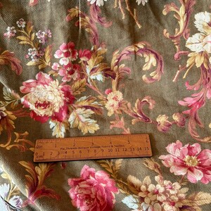 Pu&ograve; includere: Primo piano di un tessuto marrone con un motivo floreale. Il tessuto presenta un disegno floreale rosa, bianco e giallo su sfondo marrone. Un righello di legno &egrave; posizionato sul tessuto, mostrando le misure in pollici e centimetri.