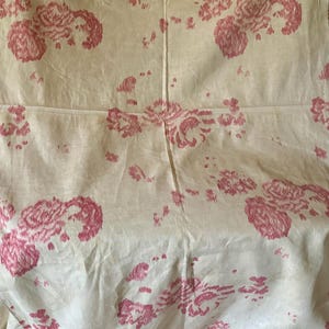 以下が含まれることがあります： クリーム色の生地に、ピンク色の花柄が繰り返されています。花は様式化され、表面に散らばっており、ヴィンテージ感を醸し出しています。生地は軽く、リネンまたはコットンであるようです。