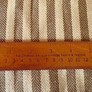 K&ouml;nnte beinhalten: Nahaufnahme eines Stoffes mit braunem und cremefarbenem Fischgr&auml;tmuster. Ein Holzlineal, in Zoll und Zentimetern markiert, liegt auf dem Stoff. Das Lineal tr&auml;gt die Aufschrift "Pio Threads Antique Vintage Fabric & Textiles."