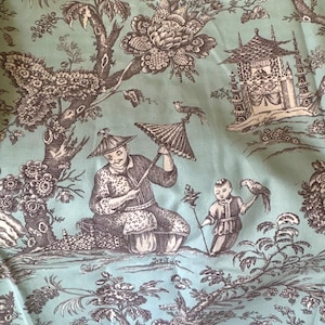 May include: A light mint green fabric featuring a dark brown toile pattern. The design depicts figures in traditional attire, one holding a parasol, alongside a child with a bird, ornate trees, floral elements, and architectural pagoda structures.