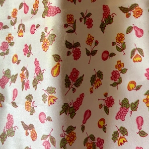May include: A white fabric with a repeating pattern of pink grapes, pears, and flowers in shades of pink, yellow, and orange. The design includes green leaves and stems, creating a colorful, botanical print.