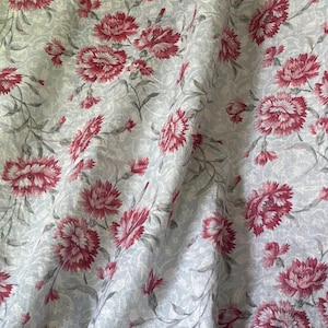 May include: A fabric featuring a repeating floral pattern of deep red carnations with dark green stems and leaves. The background is a light gray color with a dense, intricate, and swirling paisley-like texture that covers the entire surface.