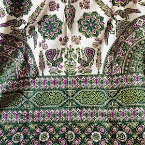 May include: A white fabric with a green and purple floral pattern. The fabric features a repeating design of peacocks, flowers, and leaves. The fabric is ideal for crafting projects, such as making curtains, tablecloths, or cushions.