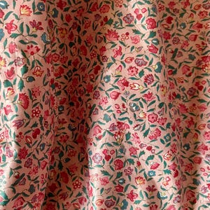May include: Pink fabric with a small floral print in shades of red, blue, and green.