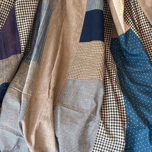 Puede incluir: Una colcha de patchwork que presenta una variedad de cuadrados y rectángulos de tela en tonos azul, marrón, beige y blanco. El diseño textil incluye patrones como cuadros vichy pequeños en blanco y negro, lunares azules y blancos y rayas.