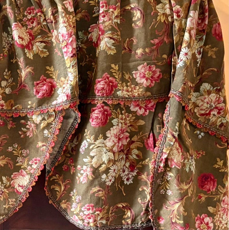 Pu&ograve; includere: Una balza in tessuto marrone con un motivo floreale con fiori rosa, bianchi e gialli. La balza ha un bordo a festoni con un bordo in pizzo marrone e rosso.