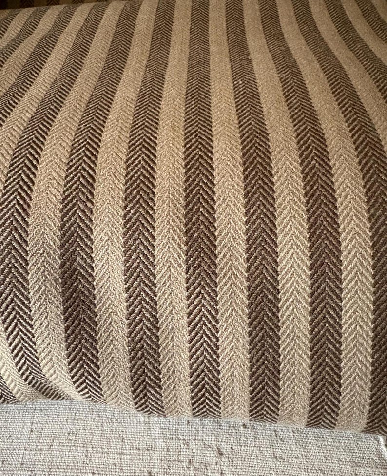 K&ouml;nnte beinhalten: Nahaufnahme eines Stoffes mit vertikalem Streifenmuster. Die Streifen wechseln sich in Hellbeige und Dunkelbraun ab. Der Stoff hat ein Fischgr&auml;tgewebe, das Textur verleiht. Geeignet f&uuml;r Polster oder Heimdekoration.