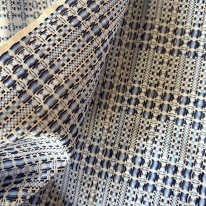 May include: Close-up of a woven fabric with a repeating geometric pattern in shades of blue and white. The fabric is folded, revealing the texture and design. The pattern includes squares, rectangles, and other shapes.
