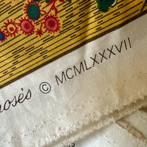 May include: Close-up of a section of fabric with a floral design in yellow, red, green, and blue. The fabric has a white border with the text "MCMLXXXVII" and the copyright symbol. The fabric is likely used for quilting or crafting.