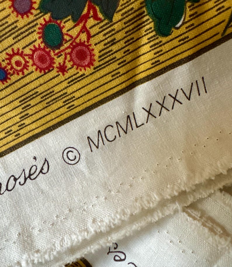 May include: Close-up of a section of fabric with a floral design in yellow, red, green, and blue. The fabric has a white border with the text "MCMLXXXVII" and the copyright symbol. The fabric is likely used for quilting or crafting.