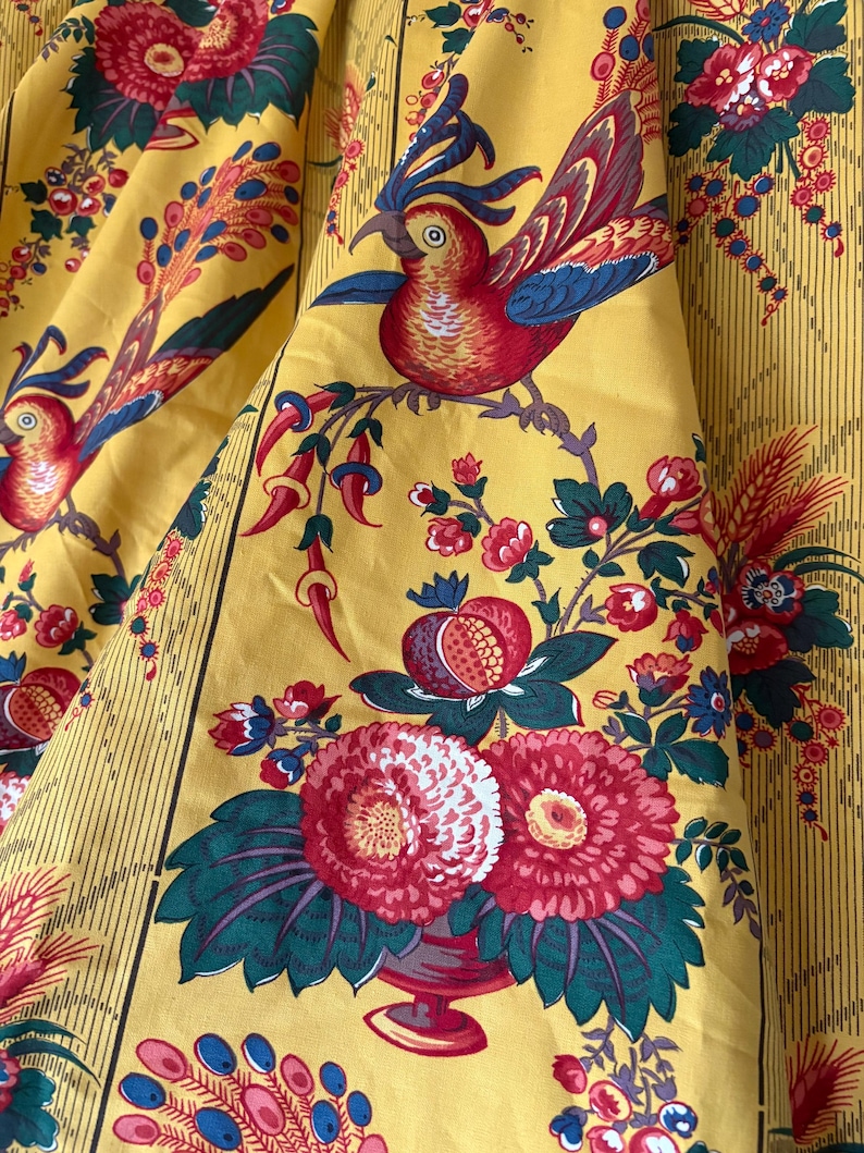 May include: Yellow fabric with a repeating pattern of red and blue birds perched on branches with flowers and fruit. The fabric has vertical stripes and a vintage aesthetic.