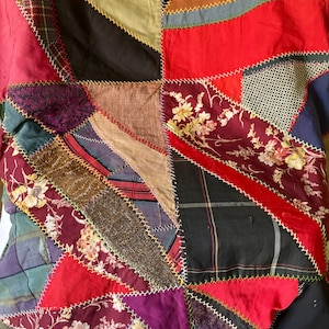 May include: A patchwork quilt with a variety of fabrics in a geometric design. The quilt features triangles and other shapes in red, black, purple, and floral patterns, stitched together with contrasting thread.