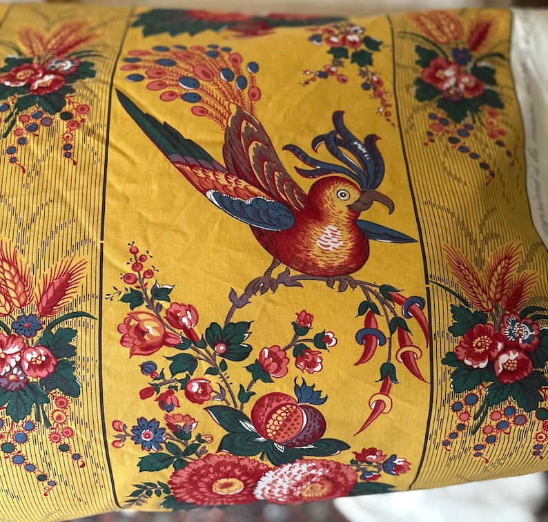 May include: A decorative pillow with a yellow background featuring a detailed bird and floral design. The bird is red, brown, and blue, perched on a branch with red and pink flowers. The pillow has a vertical striped border.