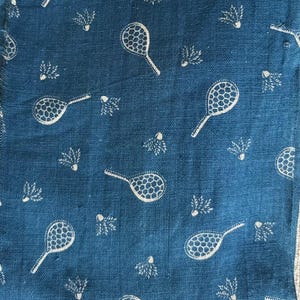 Puede incluir: Primer plano de una tela azul con un patrón repetido de raquetas y volantes de bádminton blancos. Las raquetas tienen un diseño de red detallado y los volantes tienen una apariencia de plumas. La tela tiene una apariencia texturizada.