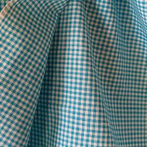 May include: Close-up of a folded fabric with a teal and white gingham pattern. The fabric is soft and has a slight sheen, with the weave visible. The pattern is a classic, small-scale check.