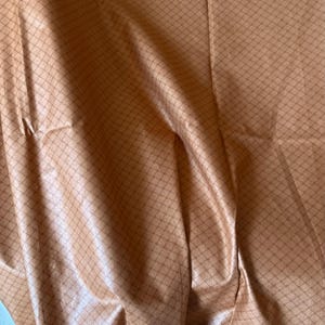 May include: Close-up of a fabric with a diamond pattern in shades of tan and brown. The fabric has a slight sheen, and the pattern is subtle. The folds and creases in the fabric add texture and depth to the image.