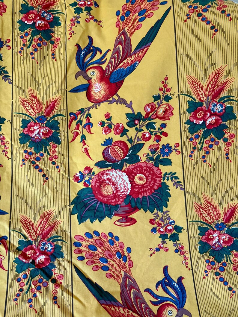 May include: Yellow fabric with a repeating pattern of red and blue birds, flowers, and foliage. The design includes vertical stripes and a variety of floral arrangements. The fabric has a vintage, decorative style.