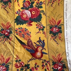 May include: Yellow fabric with a repeating floral and bird pattern. The design features red, white, and blue flowers, along with a detailed bird illustration. The fabric has vertical stripes and text that reads "&eacute;dit&eacute; par Frelle, imprim&eacute; &agrave; la main, marque et mod&egrave;le d&eacute;pos&eacute;s &copy; MCMLXXXVII".