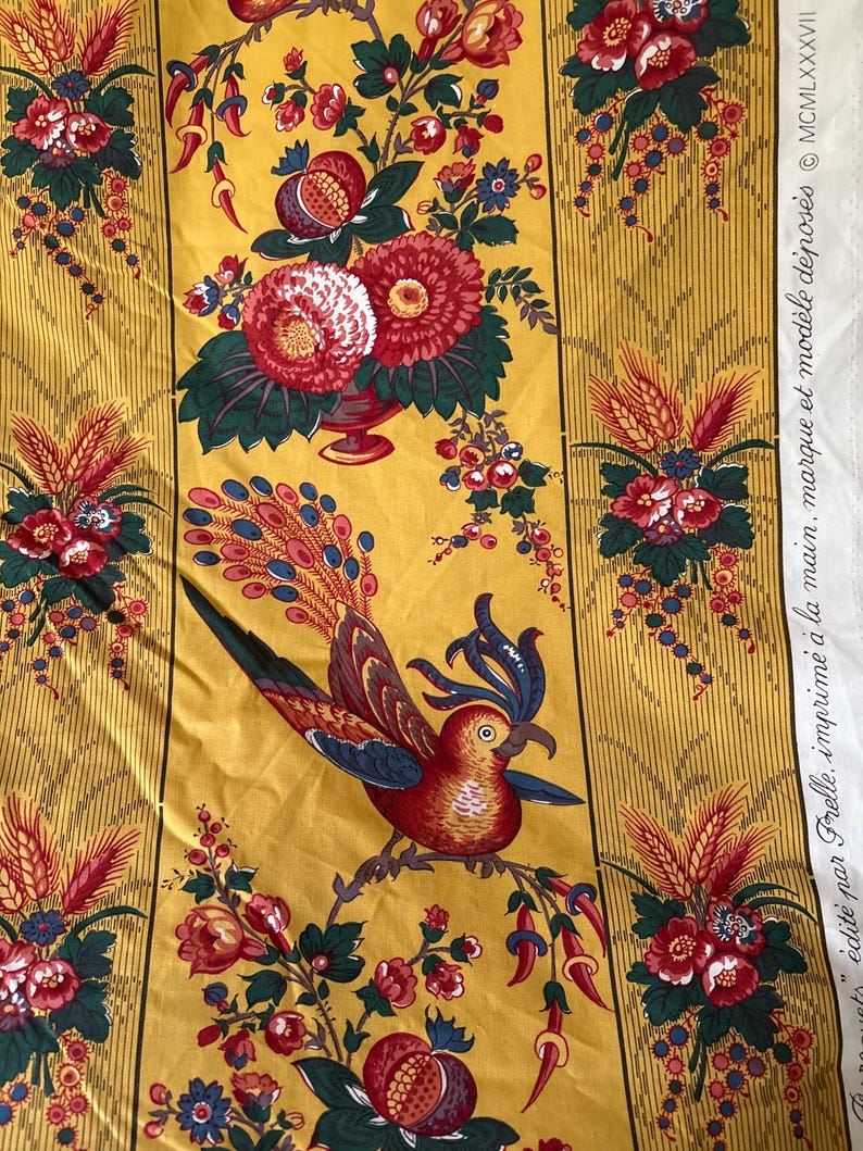 May include: Yellow fabric with a repeating floral and bird pattern. The design features red, white, and blue flowers, along with a detailed bird illustration. The fabric has vertical stripes and text that reads "&eacute;dit&eacute; par Frelle, imprim&eacute; &agrave; la main, marque et mod&egrave;le d&eacute;pos&eacute;s &copy; MCMLXXXVII".