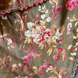 Pu&ograve; includere: Primo piano di un tessuto marrone con un motivo floreale. Il tessuto presenta un motivo floreale rosa, bianco e oro con un bordo smerlato.