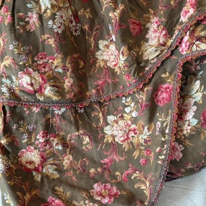 Pu&ograve; includere: Una gonna da letto in tessuto marrone con stampa floreale e bordo a balze. Il tessuto ha un aspetto e una sensazione vintage.