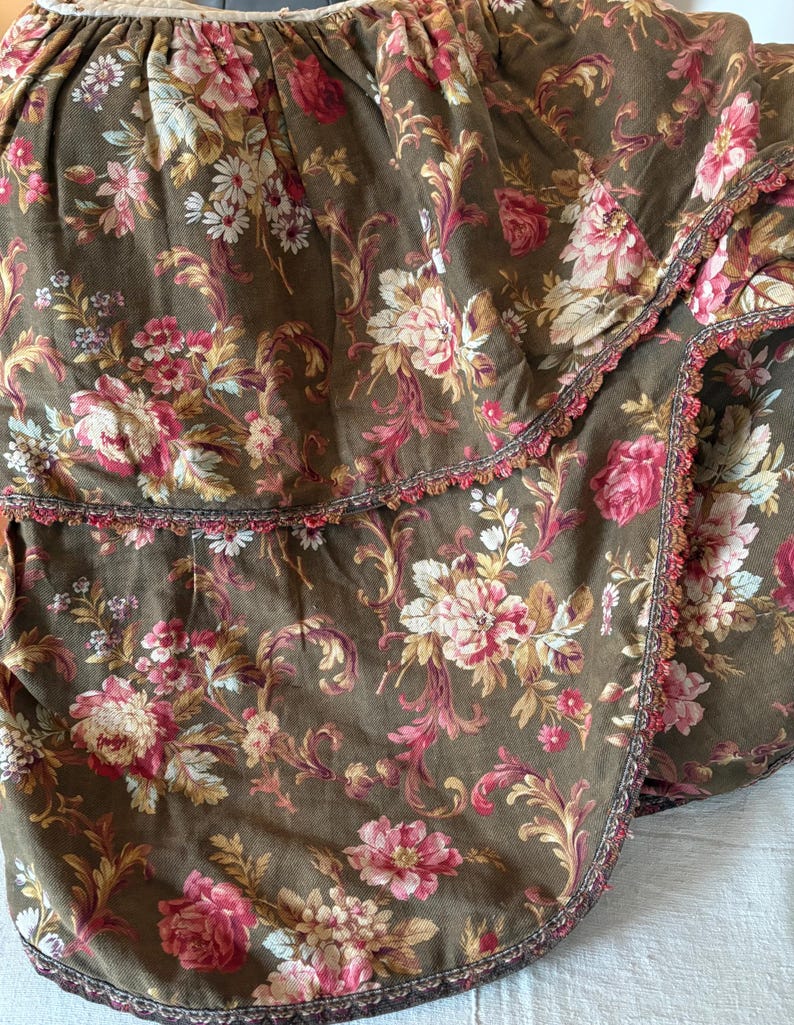 Pu&ograve; includere: Una gonna da letto in tessuto marrone con stampa floreale e bordo a balze. Il tessuto ha un aspetto e una sensazione vintage.