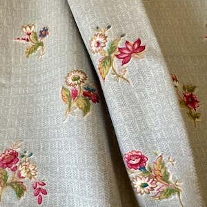 Puede incluir: Una tela gris claro con un patrón de espiga vertical repetitivo y motivos florales dispersos. Las flores bordadas están representadas en tonos rosa oscuro, rojo, blanco y verde, con pequeños acentos azules en todo el diseño textil.