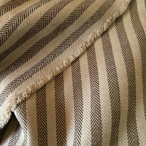 K&ouml;nnte beinhalten: Nahaufnahme eines Stoffes mit Fischgr&auml;tmuster. Der Stoff weist abwechselnd vertikale Streifen in Hellbeige und Dunkelbraun auf. Der Rand des Stoffes ist ausgefranst und gibt den Blick auf das Gewebe frei.
