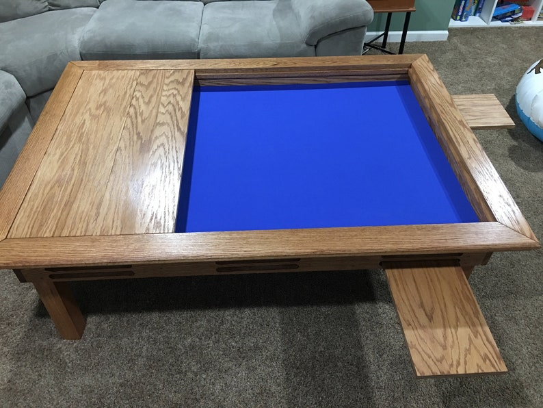 May include: A wooden coffee table with a blue felt game board insert and two pull-out side panels. The table has a natural wood finish and a rectangular shape.