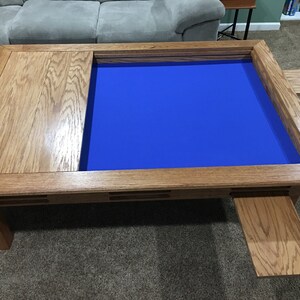 May include: A wooden coffee table with a blue felt game board insert and two pull-out side panels. The table has a natural wood finish and a rectangular shape.