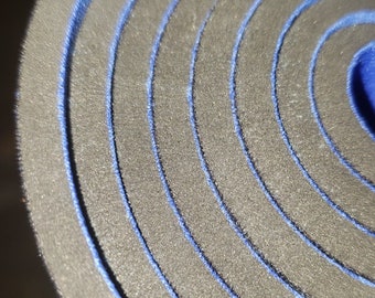 May include: Close-up of a rolled-up yoga mat with a black outer layer and blue edging. The mat is rolled up tightly, showing the layers of the mat.