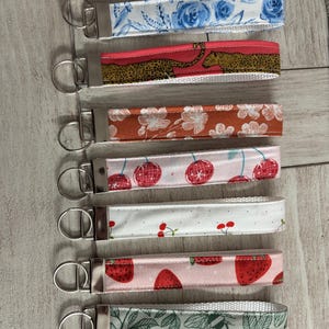 May include: Set of seven colorful keychains with different patterns. The keychains feature a variety of designs, including floral, animal print, and fruit. Each keychain has a silver metal ring.