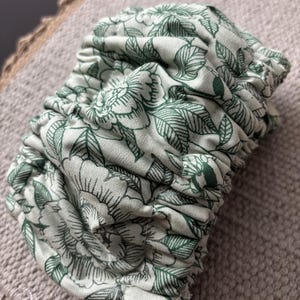 Puede incluir: Una tela floral verde y blanca con un dise&ntilde;o fruncido. La tela es suave y tiene un delicado estampado floral.